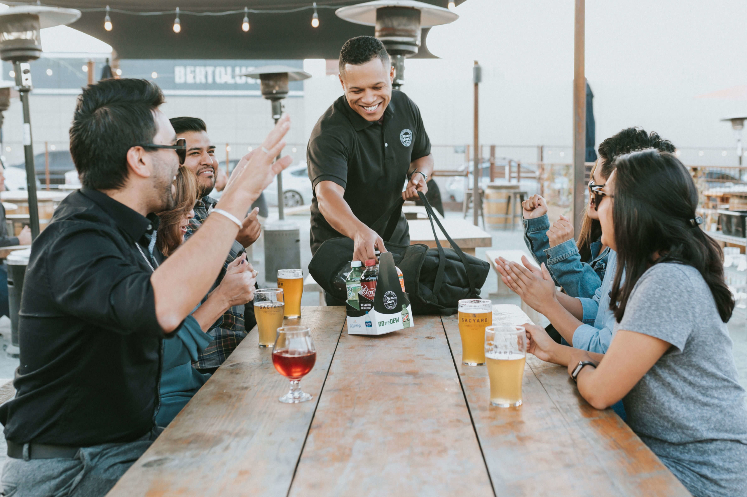 Family sitting around table enjoying drinks while server delivering pizza to table.